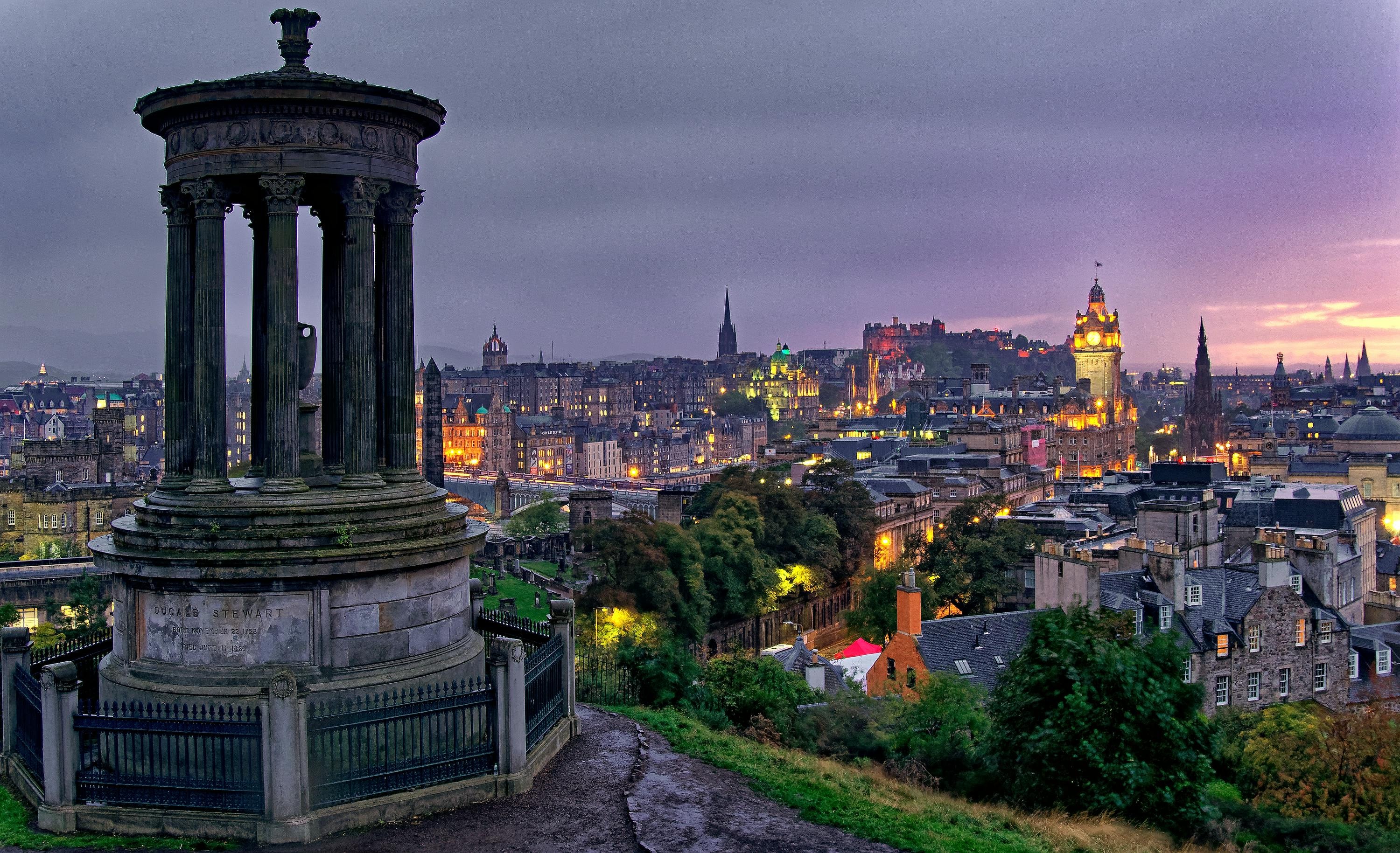 Edinburgh at dusk viewed from beside the Dugald Stewart Monument on Calton Hill, city lights beginning to glow under a purple sky